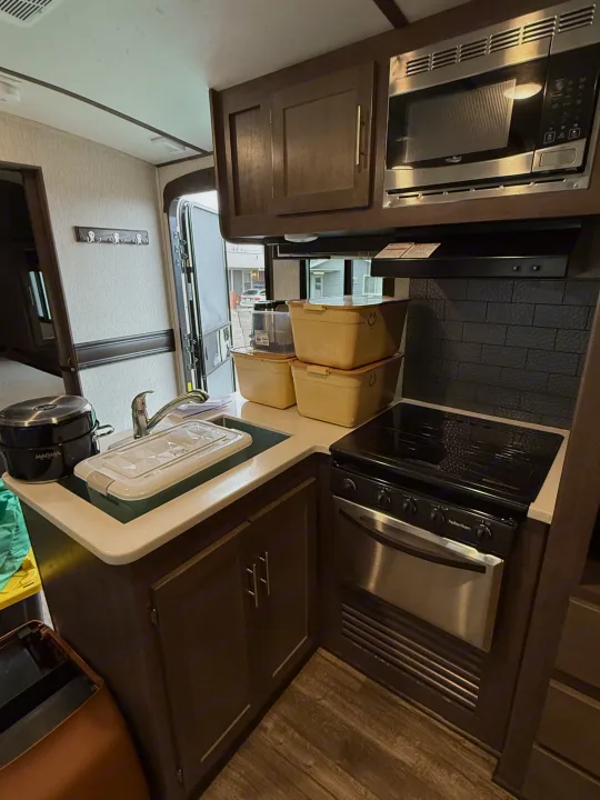 This RV rental kitchen showcases a microwave, stove, sink, and storage bins, providing essential amenities for your travels.. Crossroads Sunset Trail Super Lite 2019