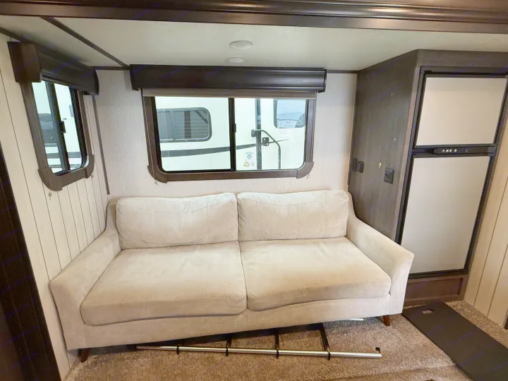 RV rental interior: A light two-seater sofa anchors the living area with large windows and a compact fridge on the right.. Crossroads Sunset Trail Super Lite 2019