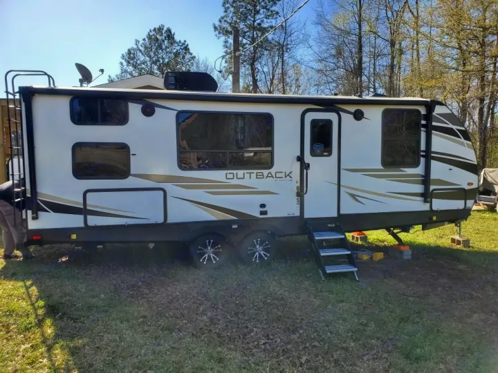 White Outback travel trailer RV rental parked on grass, ready for adventure with steps & roof antenna.. Keystone Outback 2021