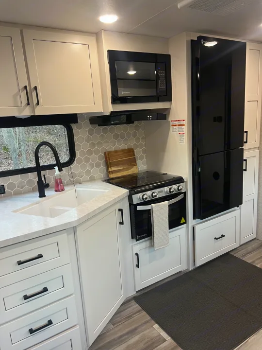 Modern RV rental kitchen featuring white cabinets, black appliances, a hexagon backsplash, and a large sink.. Jayco Jayflight 324bds 2025