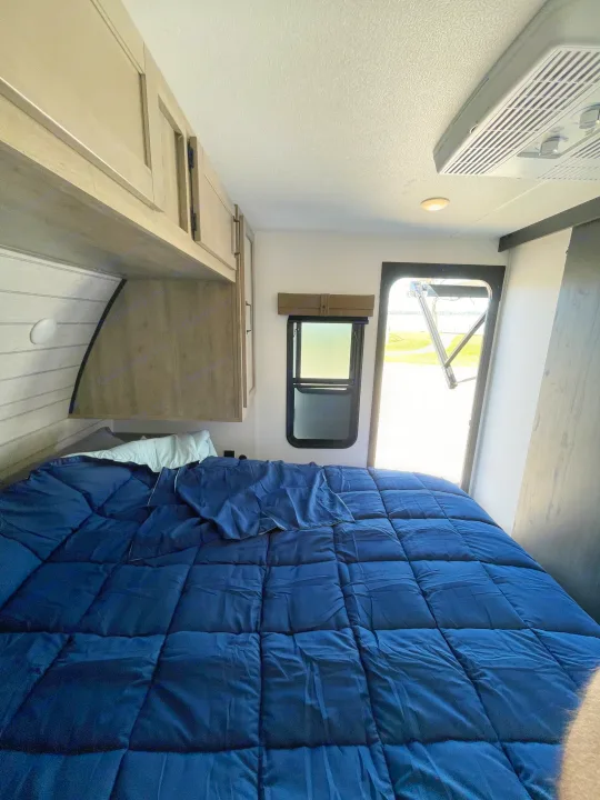 Cozy RV rental bedroom featuring a comfortable bed with blue bedding, overhead cabinets, and a bright view through the open door.. Palomino Puma 337BH 2025