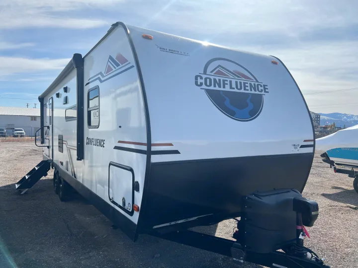 A white Confluence RV rental, a modern travel trailer, is parked with its steps down, ready for your next outdoor adventure.. KZ Confluence 2022