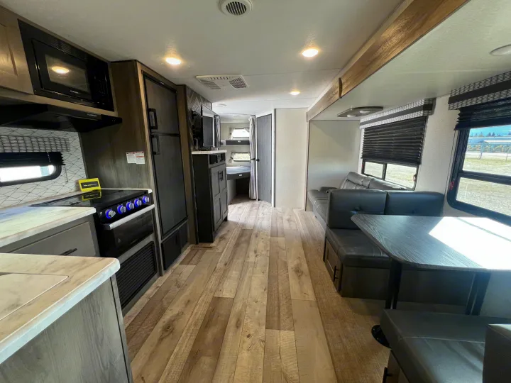 Modern RV rental interior featuring a full kitchen with microwave & stove, comfortable dinette, and wood-look floors.. KZ Confluence 2022