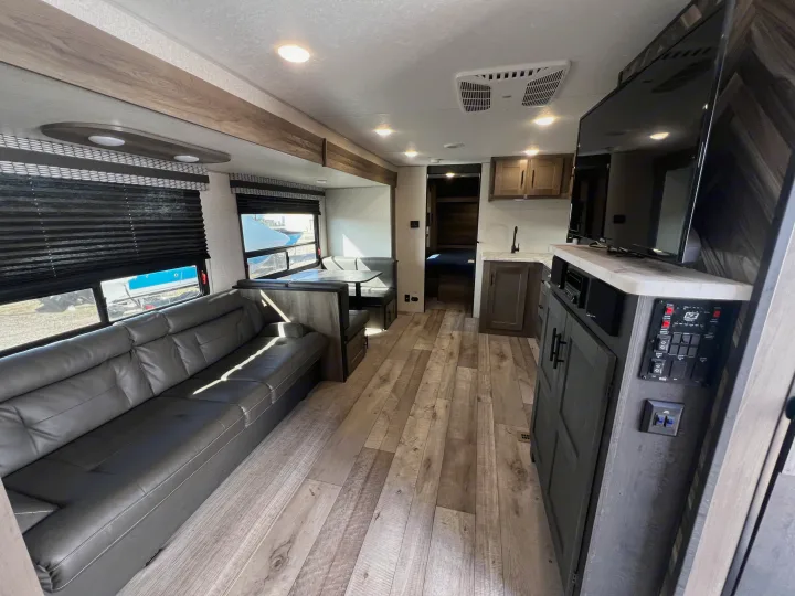 Modern RV rental interior featuring a living area with a large gray sofa, dinette, kitchen, and wood flooring.. KZ Confluence 2022