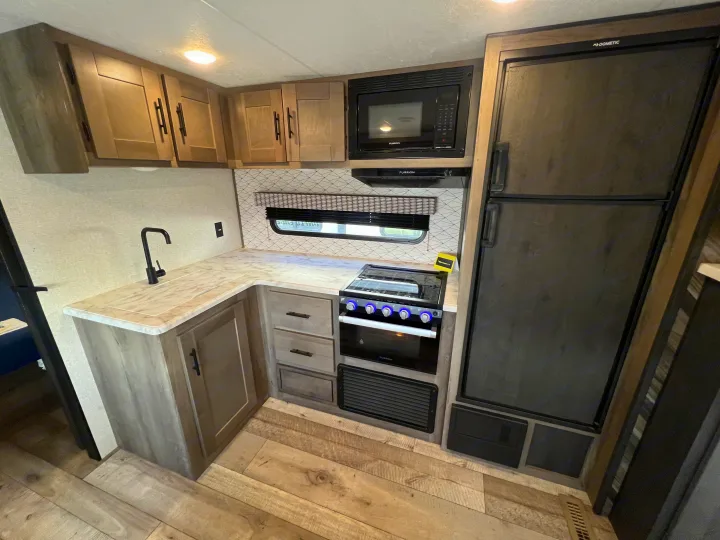 Inside this RV rental, find a compact kitchen with a black faucet, stove, microwave, refrigerator, and light wood cabinetry.. KZ Confluence 2022