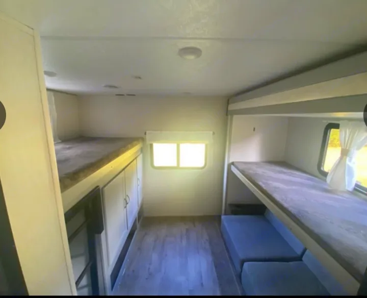 RV rental interior: Spacious bunk area with two sets of beds, including a lower sofa, built-in cabinets, and bright windows.. Forest River Vibe 2022
