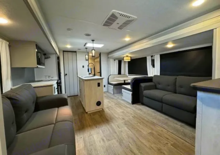 Bright RV rental interior featuring a modern kitchen, dining booth, and dual living room sofas for comfortable travel.. Forest River Vibe 2022
