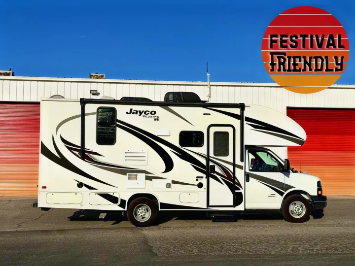 This festival-friendly Jayco RV rental, a white camper with graphic decals, is parked against a red-doored building.. Jayco Redhawk 2021