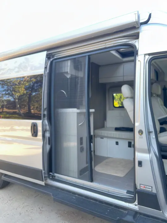 This RV rental camper van with its open side door showcases the compact interior, including a screen and versatile seating.. Thor Tellaro 2022