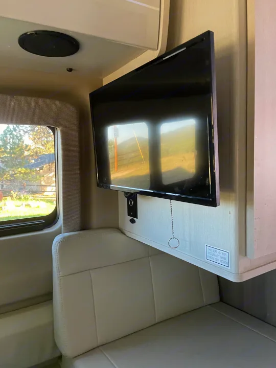 RV rental interior: Mounted TV, comfortable light seating, and a window displaying a scenic outdoor view.. Thor Tellaro 2022
