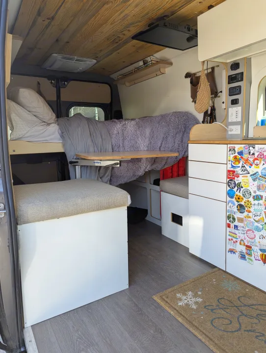 RV rental interior: wood ceiling, bed, adjustable table, control panel, and sticker-adorned storage for a cozy, functional space.. Dave & Matt Vans Dave & Matt Vans Class B 2024