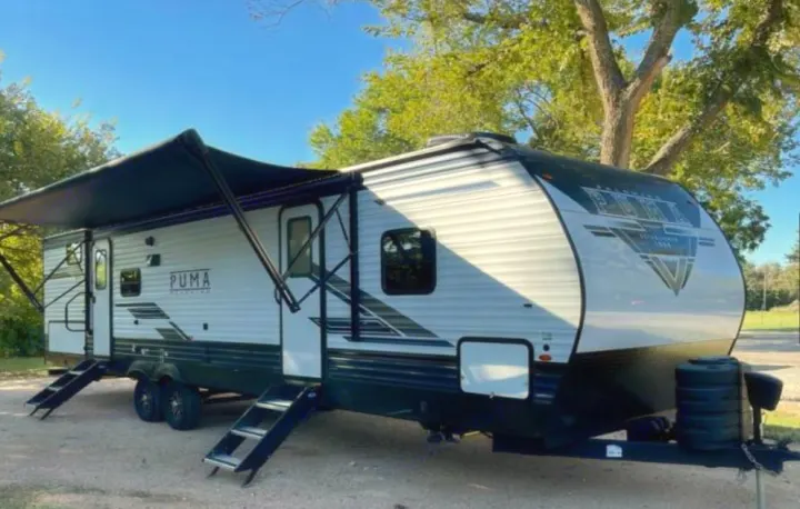 Puma travel trailer, a white and dark gray RV, ready for rv rental. Features an extended awning and dual entry steps.. PALOMINO 28BHSS 2024
