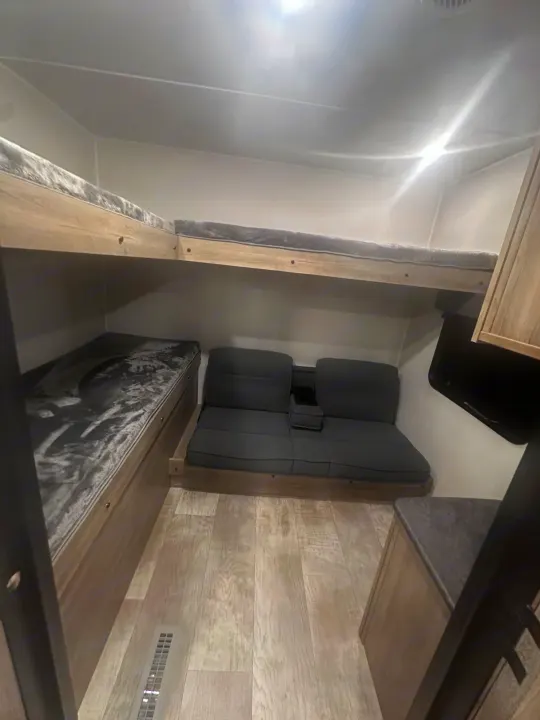 RV rental interior featuring modern bunk beds with grey bedding, a comfy sofa/dinette, and light wood-look flooring.. PALOMINO 28BHSS 2024