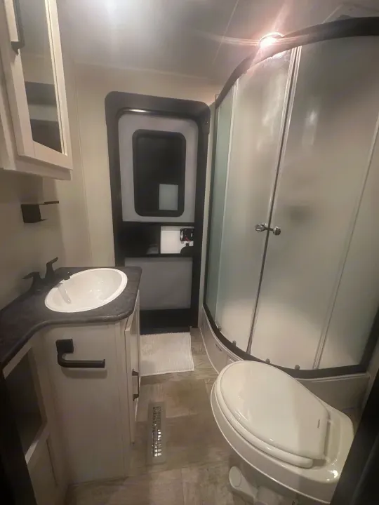Clean and compact RV rental bathroom, featuring a sink, vanity, toilet, and curved shower. Ideal for your mobile adventures.. PALOMINO 28BHSS 2024