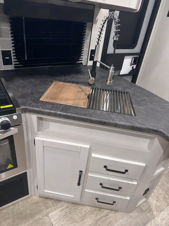 Modern RV rental kitchen featuring a sleek sink, integrated cutting board, oven, and stylish white cabinets.. PALOMINO 28BHSS 2024