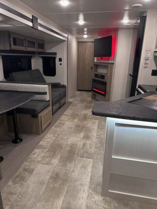 Modern RV rental interior with dinette, kitchen, fireplace, and ambient red lighting, showcasing the living space.. PALOMINO 28BHSS 2024