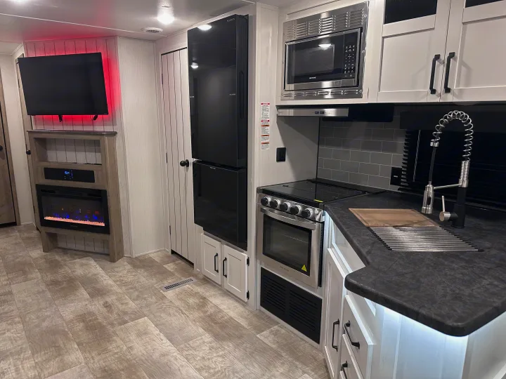 Inside a modern RV rental: a kitchen with oven, microwave & sink, and living area with TV & electric fireplace. Wood-look flooring.. PALOMINO 28BHSS 2024