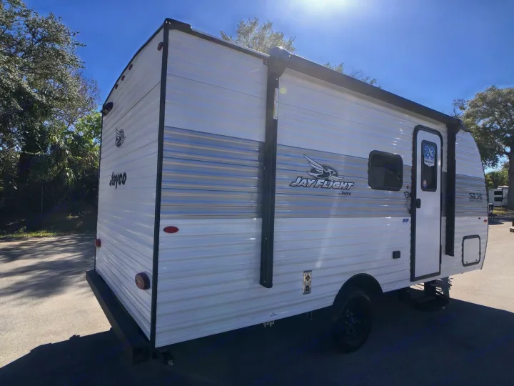 White and grey Jayco travel trailer, ready for RV rental. View of the side, featuring an awning and entrance.. Jayco Jay Flight SLX 2025