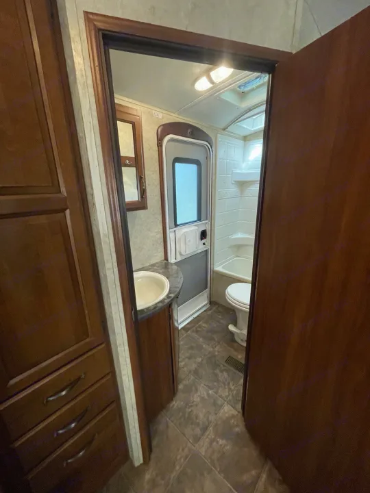 RV rental bathroom with sink, toilet, shower, and wood cabinetry.. Keystone RV Cougar 2012