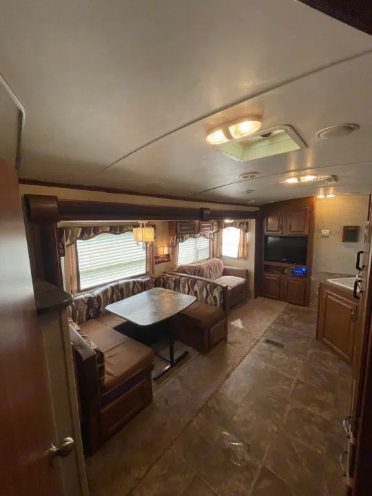 Explore this cozy RV rental interior with a U-shaped dinette, kitchen, and entertainment area. Ideal for travel adventures.. Keystone RV Cougar 2012