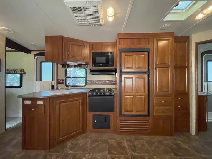 Step inside this RV rental's well-equipped kitchen area, showcasing warm wooden cabinetry, appliances, and a compact living space.. Keystone RV Cougar 2012