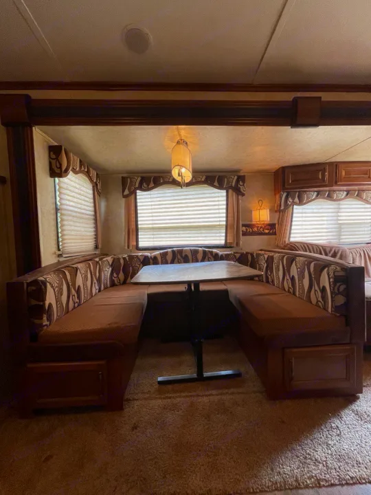 U-shaped dinette in an RV rental, showing a cozy dining area with patterned cushions, a table, and window blinds.. Keystone RV Cougar 2012