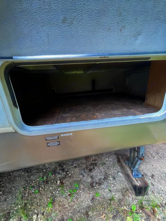 Open RV rental storage compartment. Shows interior plumbing, tiled floor, and labels for black tank & sewer connection.. Keystone RV Cougar 2012