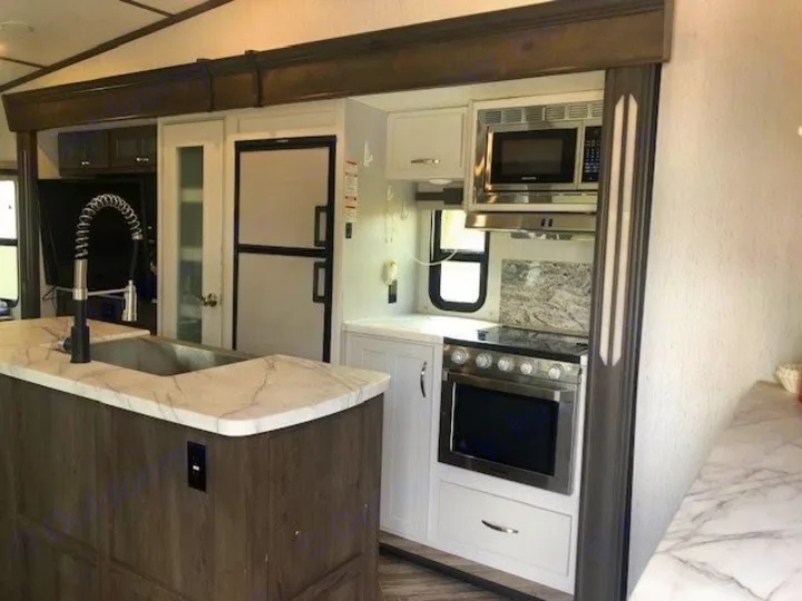 This spacious RV rental kitchen features a modern island with a sink, fridge, microwave, and stove for convenient travel.. Astoria 1500 2021