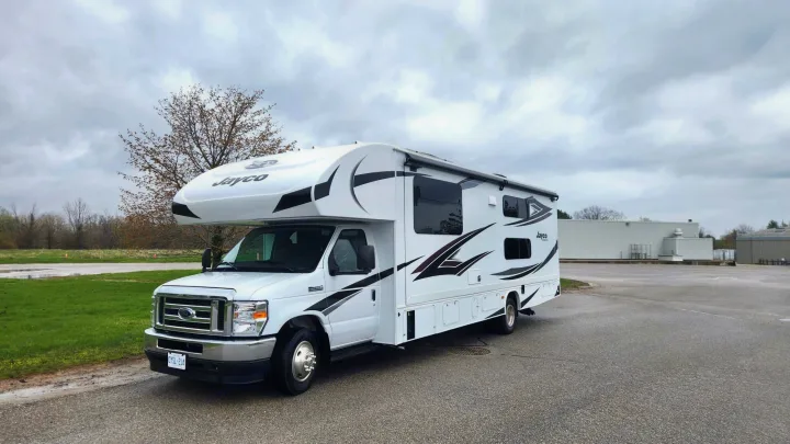 White Jayco RV rental parked on asphalt, ideal for camping & road trips. Overcast sky, tree, and buildings in background.. JAYCO REDHAWK 2023 2023