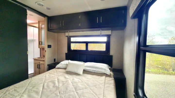Modern RV rental bedroom with a comfy bed, window view, overhead storage, and adjacent bathroom.. JAYCO REDHAWK 2023 2023