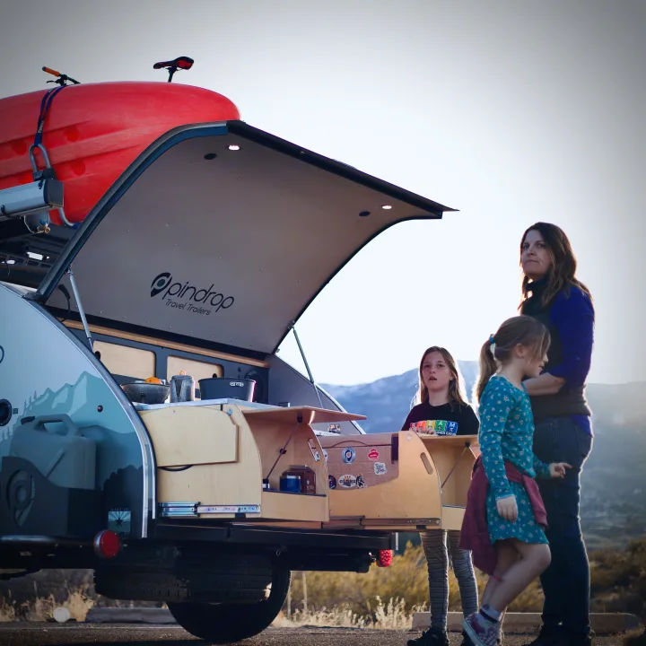 An RV rental alternative: a family with their Pindrop teardrop travel trailer and open kitchenette for camping.. Pin Drop Travel Trailers Scout 2022