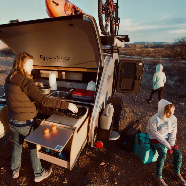 Enjoying an RV rental experience: Family cooks outdoors from their Pindrop teardrop camper, ready for adventure.. Pin Drop Travel Trailers Scout 2022
