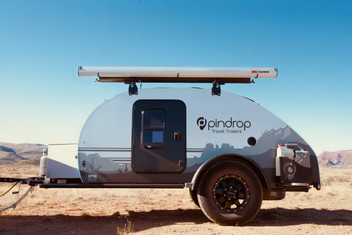 A white and grey Pindrop teardrop RV with a roof awning, parked in a vast desert, ideal for rv rental.. Pin Drop Travel Trailers Scout 2022
