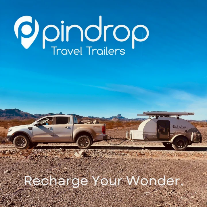 A white truck tows a Pindrop travel trailer in a vast desert. Explore with this compact RV rental for your next outdoor adventure!. Pin Drop Travel Trailers Scout 2022