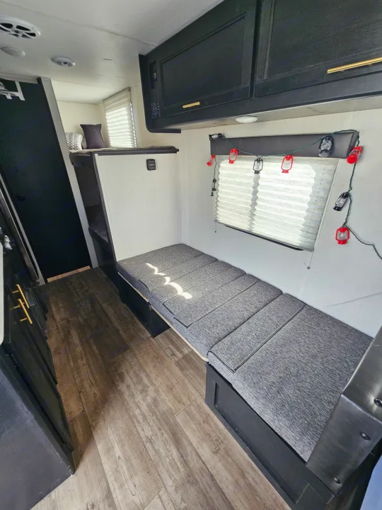 Bright and clean RV rental interior with convertible bench bed, black cabinets, and wood-patterned floor.. Forest River Cherokee Wolf Pup 2022