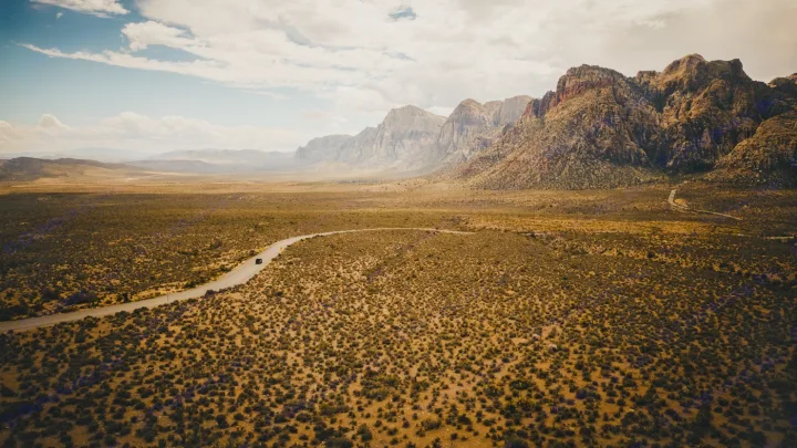 An RV rental drives through Red Rock Canyon-like desert, a winding road leading to majestic mountains under a vast sky.. Toyota Other 2025