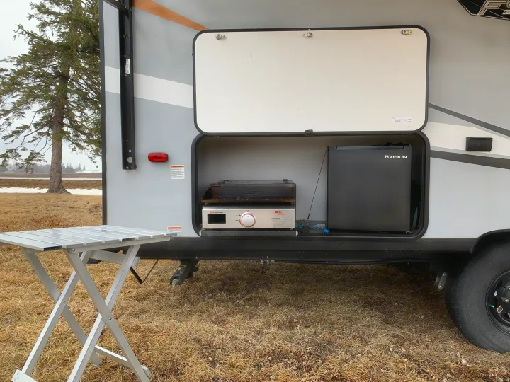 Outdoor kitchen setup for your next RV rental adventure, featuring a grill, fridge, and folding table.. Forest River Wildwood FSX Plantium 2022