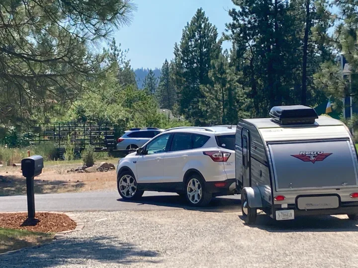 White SUV with a 'Retro Jr.' teardrop RV rental attached, parked on a sunny driveway near a mailbox and trees.. Riverside RV Retro 2017
