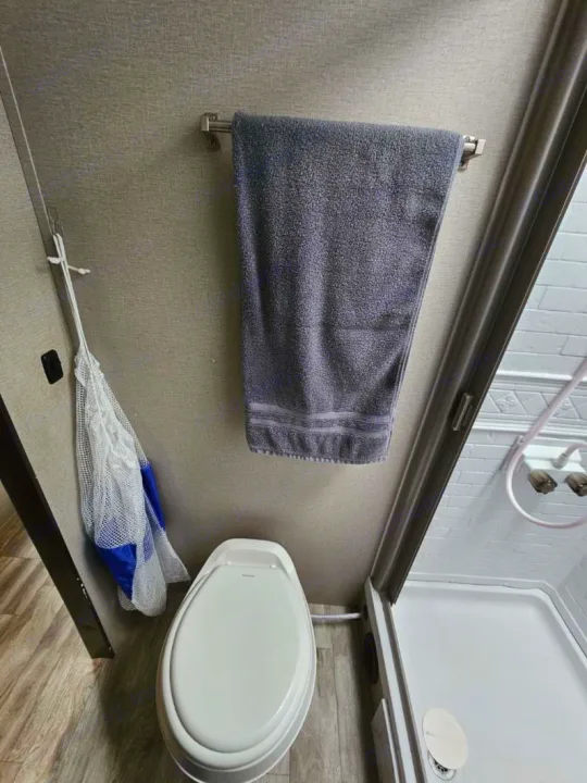 An efficient RV rental bathroom featuring a white toilet, a gray towel on a wall bar, and a compact shower stall.. Grand Design Transcend Xplor 2022