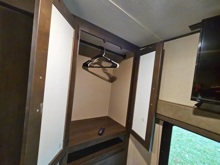 Compact RV rental wardrobe: Features a hanging rod, shelf with remote, and white doors, providing essential storage in a tight space.. Grand Design Transcend Xplor 2022