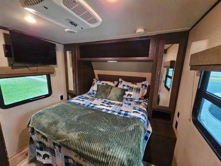 Cozy RV rental bedroom with bear-themed bedding, a wall-mounted TV, overhead AC, and storage cabinets.. Grand Design Transcend Xplor 2022