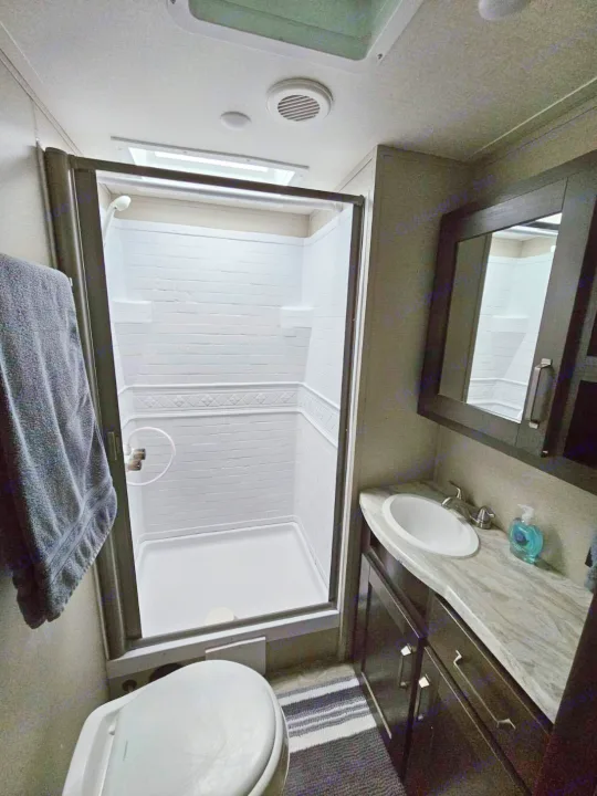 Compact RV rental bathroom with a white shower, toilet, and dark vanity featuring a modern sink.. Grand Design Transcend Xplor 2022