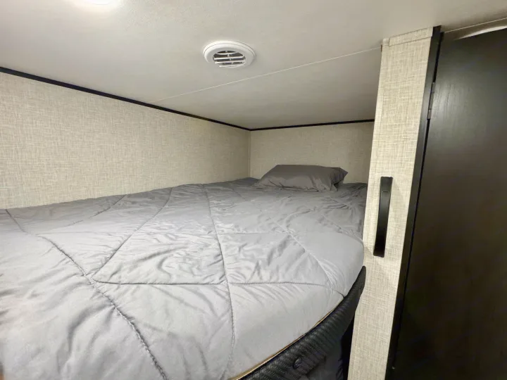 Cozy RV rental bunk bed with a grey comforter, pillow, and overhead vent for comfort.. Jayco 260BH 2025