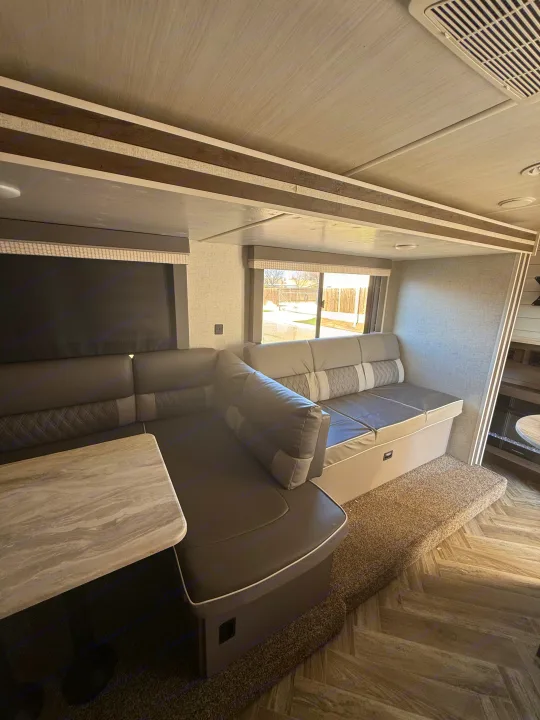 Spacious RV rental interior featuring a modern U-shaped dinette with comfortable gray seating, a table, and large window views.. Forest River Salem Cruise Lite 2022