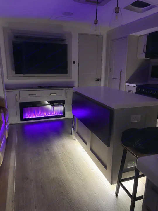 Modern RV rental interior featuring a cozy electric fireplace and kitchen island with ambient lighting.. Brinkley 295 AIR 2025