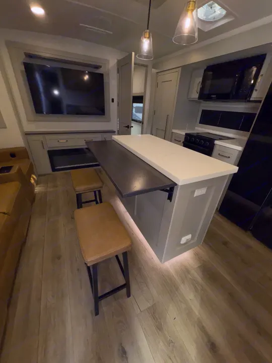 Modern RV rental interior: kitchen island with seating, TV, fireplace, and full appliances for a comfortable travel experience.. Brinkley 295 AIR 2025
