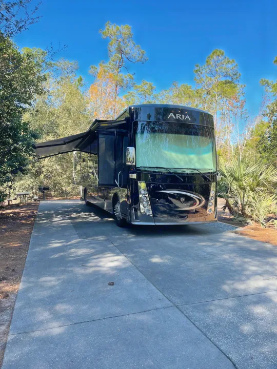 This black Aria RV rental is perfectly set up at a sunny campsite, with an extended awning and nearby picnic area.. Thor Motor Coach Aurora 2020