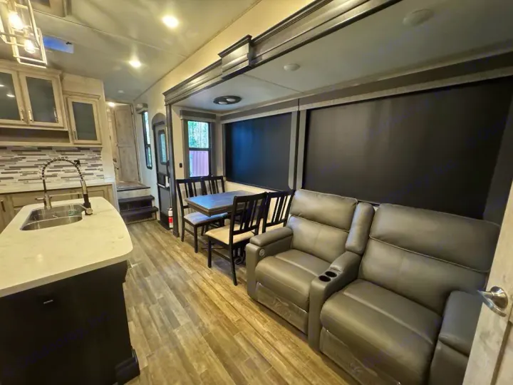 Inside a premium RV rental: spacious living area with kitchen island, dining table, & recliners.. Keystone RV Avalanche 2022