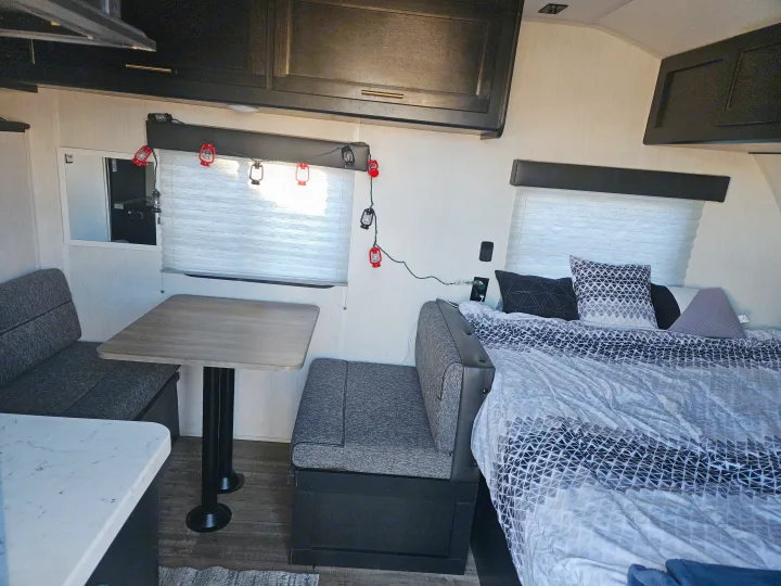 RV rental interior showcasing a dinette with seating and table, a comfortable bed with patterned bedding, and dark overhead cabinets.. Forest River Cherokee Wolf Pup 2022