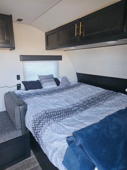 A modern RV rental bedroom with geometric bedding, dark cabinets, and a comfortable bench seat provides ample comfort.. Forest River Cherokee Wolf Pup 2022